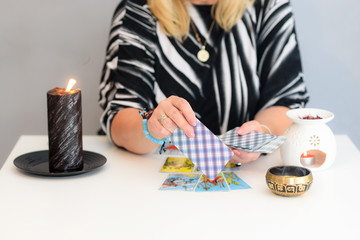 Middle age beautiful woman sits near a fortune teller desk with a Tarot cards and candles. Card...