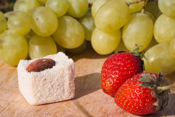 Candy and fruit on a wooden board. Grapes, strawberries and almonds.