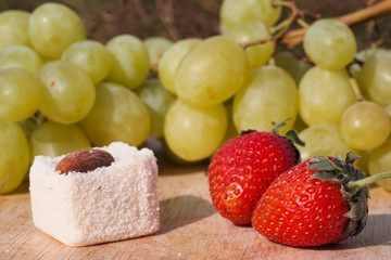 Candy and fruit on a wooden board. Grapes, strawberries and almonds.