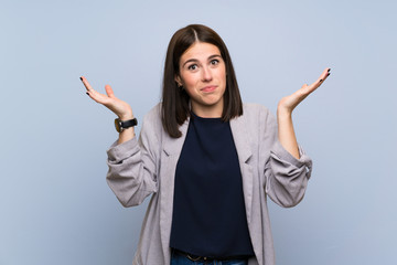 Young woman over isolated blue wall making doubts gesture