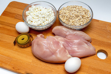 raw chicken breast, cereals, eggs, measuring tape, farm cottage cheese close up on wooden background protein healthy diet concept eco product sports nutrition