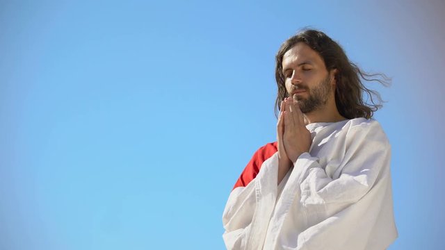 Man in robe praying to God against blue sky background, asking soul salvation