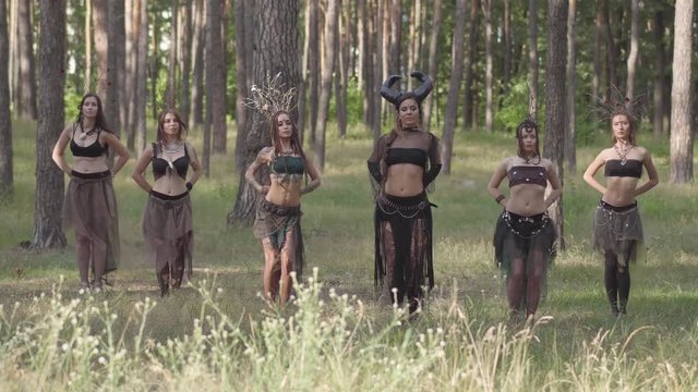 Young women in beautiful costumes of dryads or forest nymphs showing performance in an enchanted forest or making ritual under the trees