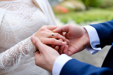 wedding details - Groom wears bride wedding gold ring at ceremony outdoor in spring time
