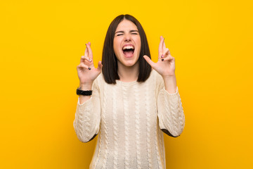 Young woman over isolated yellow wall with fingers crossing