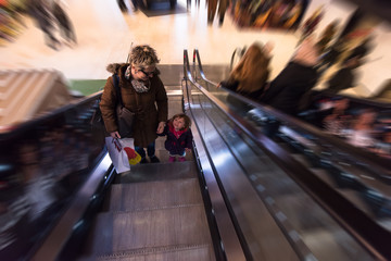 young mother and her little daughter on escalator in shopping mall