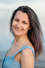 A young attractive dyed hair woman, in a blue dress, walks along the seashore. Portrait of a smiling woman on vacation with a glass of wine.