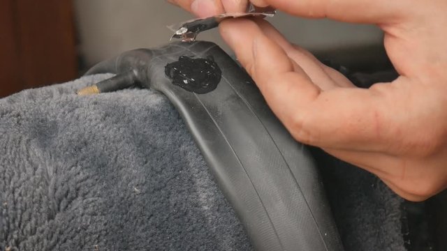 Cyclist or mechanic is applying glue on punctured inner tube. Close up of hands and bicycle flat tire tyre. A man repairs a bicycle wheel pierced.