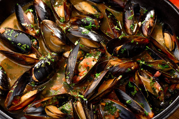 Mussel shells in cream sauce in a black cauldron on a dark wooden background, decorated with vegetables