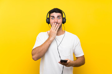 Young handsome man listening music with a mobile over isolated yellow wall with surprise facial expression