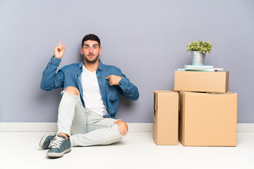 Handsome young man moving in new home among boxes with surprise facial expression