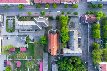 View of the city block from above. Roofs of houses and a Catholic church in the center. Among the houses on the road drive cars. Snapshot from the drone.