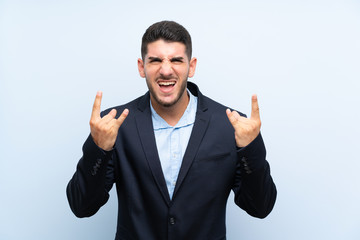 Handsome man over isolated blue background making rock gesture