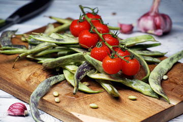 Greenbeans and cherry tomatoes in a wooden board on a rustic table.
