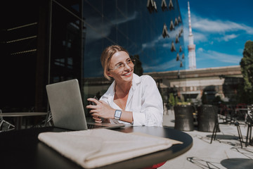 Cropped photo of smiling businesswoman sitting at table and working at laptop