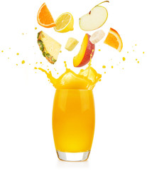pieces of fruit falling into a yellow juice glass splashing on white background