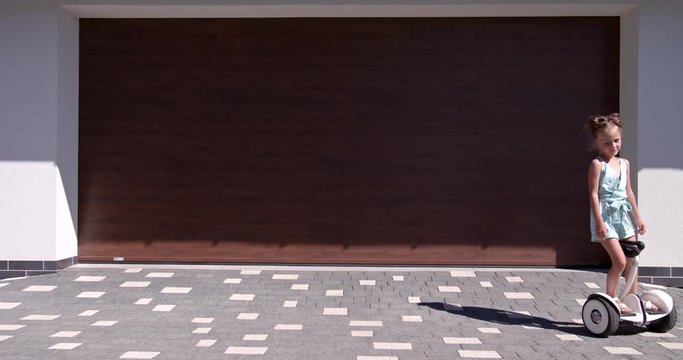 Little Girl rides a gyroscooter near the garage