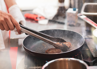 Fry the meat in a frying pan. Chef preparing and spicing meat restaurant kitchen