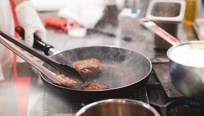 Fry the meat in a frying pan. Chef preparing and spicing meat restaurant kitchen