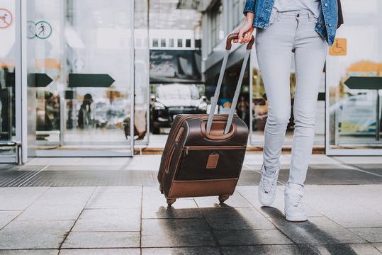 Cropped photo of woman walking with suitcase on wheels inside of airport