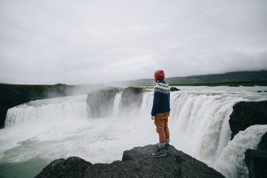Epic and amazing landscape of nordic country, iceland or norway. Adult man, travel blogger or curious tourist stand on edge of steep dangerous cliff next to raging huge waterfall