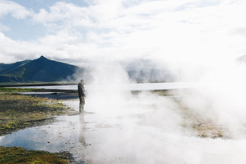 Tourist or traveller stands on edge of volcanic lake or geiser in iceland. Steam and gas evaporates into cold air. Amazing natural wonder. Scandinavian roadtrip and travel destination wanderlust