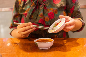 Hand holding chopsticks putting chili and garlic in Japanese sauce for eating with grilled meat