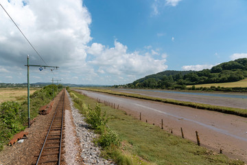 Fototapeta na wymiar Seaton, Devon, England, UK. July 2019. Tramway tracks run alongside the River Axe at low tide looking towards Axmouth, Devon.
