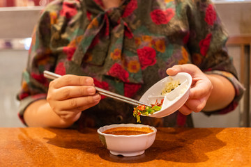 Hand holding chopsticks putting chili and garlic in Japanese sauce for eating with grilled meat
