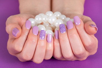 Beautiful female hand with a lilac color manicure holding pile of pearls isolated on purple background in the studio. Manicure and beauty concept. Close up, selective focus