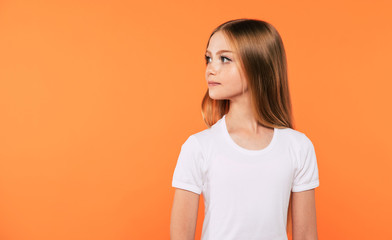 Obraz premium Side view portrait of beautiful little blonde girl in white t-shirt is posing isolated on yellow background