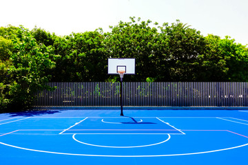 Basketball court in an outdoor park, with intense midday sun, nobody, and blue painted floor.