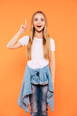 Great idea! Cute happy blonde girl shows her finger up and looks on camera standing against yellow wall