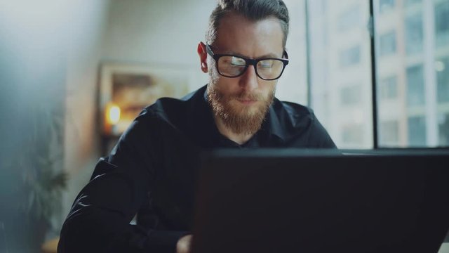 Bearded businessman man working at sunny office on desktop computer while sitting at wooden table.