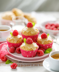 Muffins with white chocolate, fresh raspberries and mint on a ceramic plate on a wooden white...
