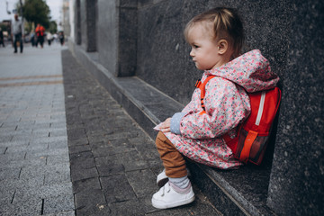 little pretty baby who got lost in the city, a girl in a pink raincoat, with a backpack and a...