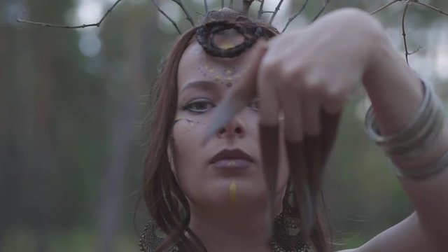 Portrait of an attractive dryad or forest fairy with a wreath of branches on the head and painted the third eye on the forehead dancing under the trees. Ancient ritual of forest creature. Slow motion.