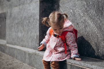 little pretty baby who got lost in the city, a girl in a pink raincoat, with a backpack and a...