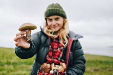 Young beautiful woman in camping outdoor outfit for cold harsh weather holds out wild fresh picked...