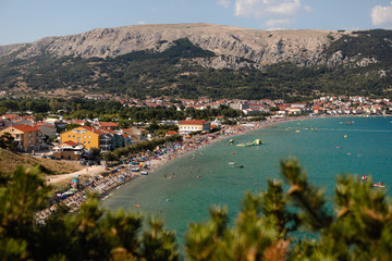 Fototapeta na wymiar Adriatic Sea coastline in Croatia. Rocky shore with turquoise sea water. Baska island, touristic destination in Croatia. Mountains in the background. First plan in defocus.
