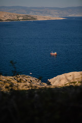 Fishing boat on dark blue water returning with lots of seagulls feeding at the rear of the boat. cliff in the foreground. first plan in defocus.