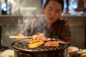 Grilling sliced pork and beef over stove in Japanese style with blurry woman in background