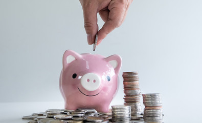 hand putting a coin into pink piggy bank with coins pile