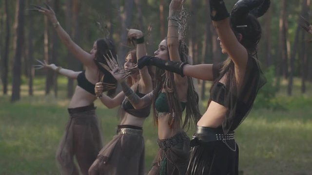 Group of women dancers with make-up and in mystical fabulous costumes dancing groovy dance in color smoke. Forest fairies, dryads have fun among the trees. Performance of dancers outdoors. Slow motion