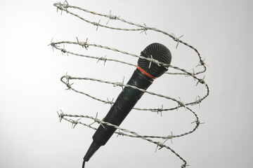Mic enclosed in barbed wire. Censorship concept of the press. Isolated on grey background. With...