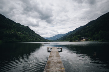Landscape shot of pristine clean alpine lake in mountain forest on cloudy and rainy day, untouched clear water reflects clouds. Wooden pier reaches out, perfect location for meditation and yoga