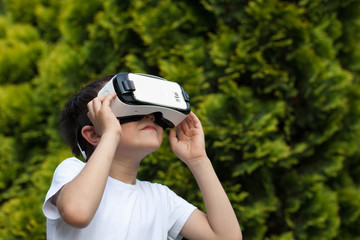 Cute little boy using VR glasses outdoors in a park - Blogger testing augmented reality goggles...
