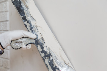 Worker in white gloves performs plastering of the walls of the room.