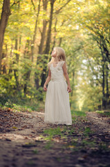 adorable blond girl walking in sunny day in magical forest