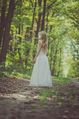 adorable blond girl walking in sunny day in magical forest